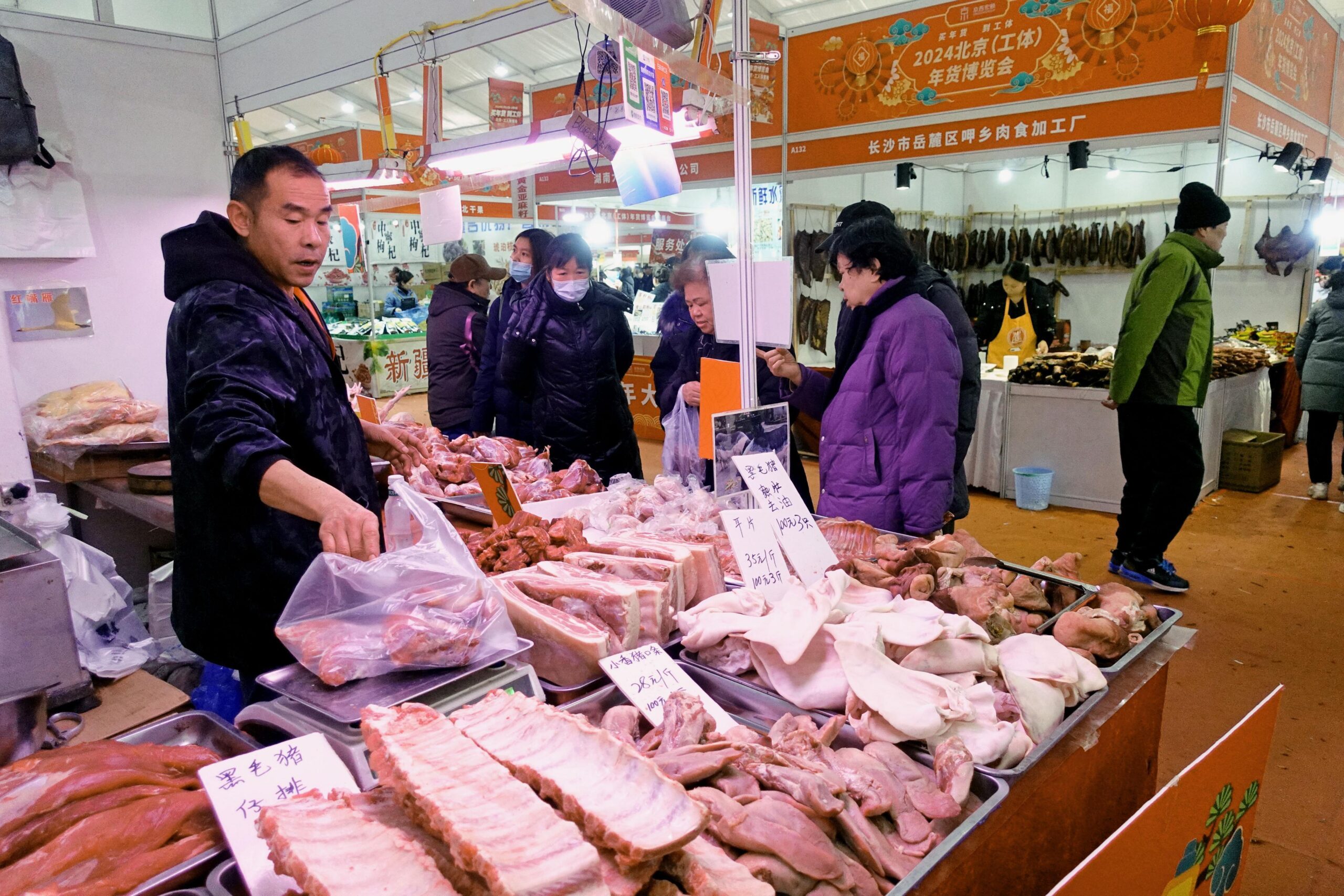 中国国家統計局が発表した2023年12月の消費者物価指数は前年同期比0.3％下落し、3カ月連続のマイナスとなった。中国経済の先行きを懸念し、多くの人々が支出に消極的だ。写真は春節用の物産展で豚肉を販売するブース＝2024年1月、北京（共同通信）